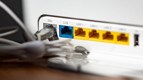 A grey LAN cable is plugged into the grey DSL slot of a white WLAN router, yellow, blue slots