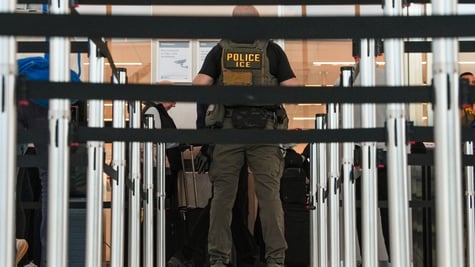 An Ice immigration agent with black security banners in front of him.