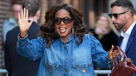 Oprah Winfrey waves right hand, jeans jacket, brown purse, brown sunglasses, white man, 