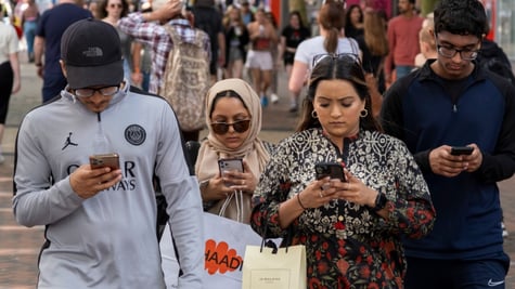 four light brown skin people, looking at smartphones, grey shirt, paper shopping bags, sunglasses 