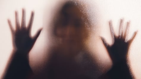 A shadow of a rape victim behind glass.