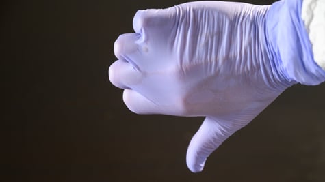 A scientist with a latex glove giving a thumbs down gesture.