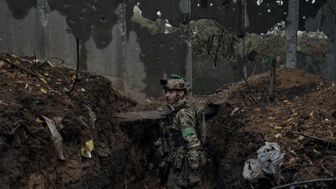 ukrainian soldier in muddy trench, uniform, muddy face, ruins around, gun on shoulder, helmet
