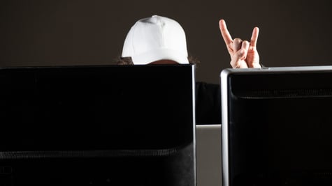 white baseball hat on head behind two black screens, rock and roll fingers in the air