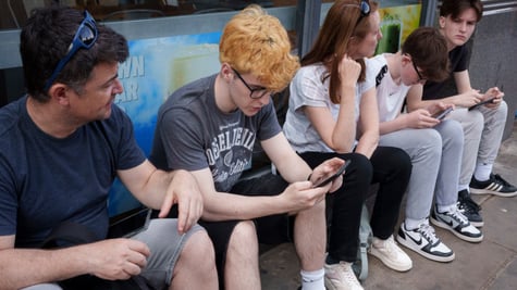 yellow curly hair, young white teen, grey tshirt, smartphone, three other people, glasses