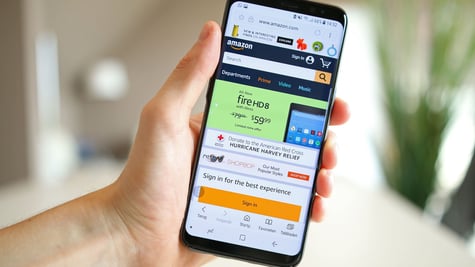 A hand holds a smartphone with an open Amazon page