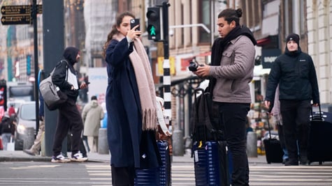 male and female tourists, darker skin, black smartphone, two dark blue luggages, pedestrian