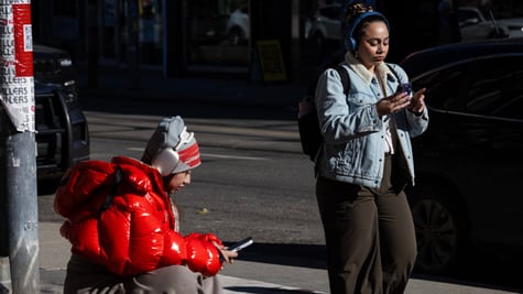woman, red puffy jacket, woman i nblack pants, light blue jeans jacket, two smartphones, scroll