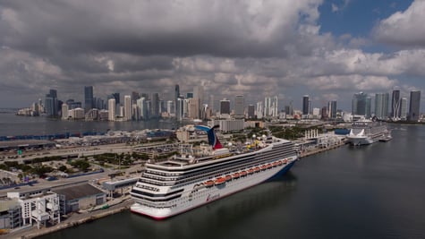 huge white Carnival cruise ship Sunrise docked in post, cloudy blue sky, miami shore, tall homes