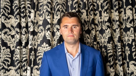 Charlie Kirk standing in front of a decorative curtain.