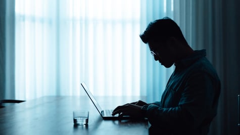 man profile from left, blue lighting, desk, light curtains, laptop, 
