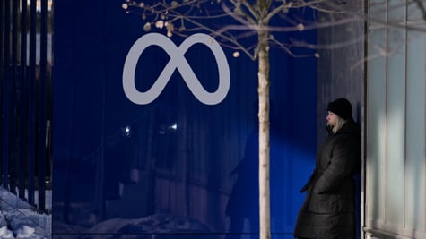 dark grey meta logo on dark blue wall, winter, woman in long black winter coat, blonde, 