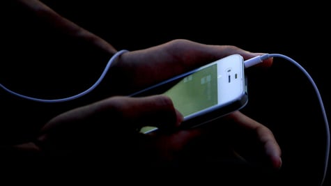 white iphone, green screen, plugged in headphone white wire, hands taping screen, darkness