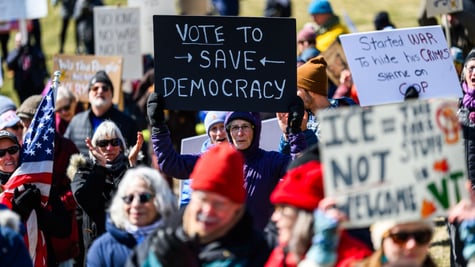 crowd of people holding protest signs, black sign, white letters, vote to save democracy