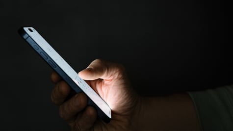 white phone screen held inright hand, shown from profile, dark room