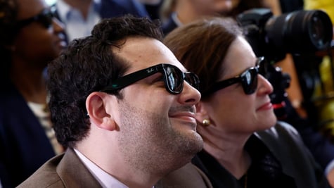 white man, chubby cheeks, dark curly hair, smiling, black ray-ban sun glasses, white woman