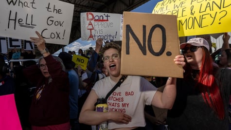 white woman, short curly blonde hair, protest signs, many people, yellow framed glasses