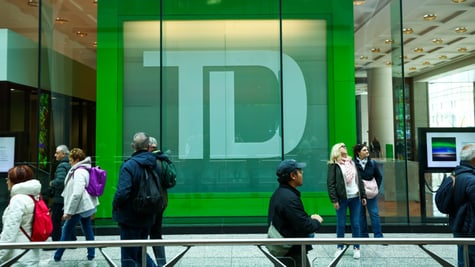 TD bank logo in green behind glass wall, about ten pedestrians walking in warm clothes