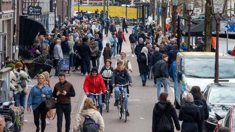busy street filled with white pedestrians, cyclists, red jacket, water canal, blue jeans jacket