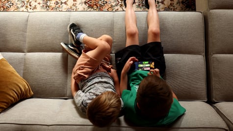 two white boys, green t-shirt- black shorts, grey t-shirt, light grey sofa, roblox on iphone screen