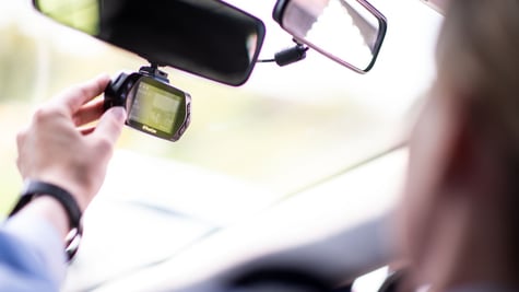 black dash camera attached to rear view window, white male hand, baby blue sleeve