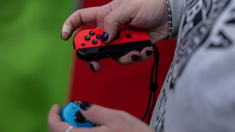 nintendo joy con held in white female hands, grey jumper, grass green background