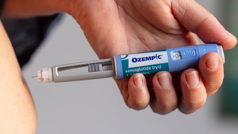 white person belly, white hand, baby blue ozempic pen, grey wall