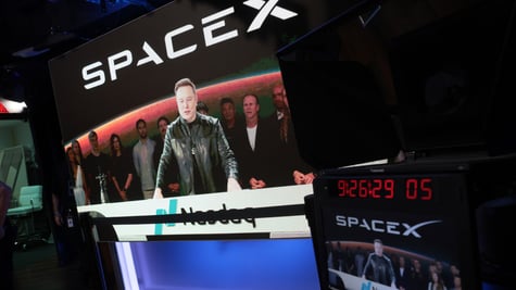 spaceX logo, elon musk on big screen, taking in video, black jacket, nasdaq