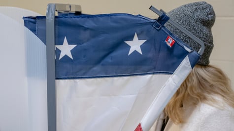 voting machine, blue and two white stars, blonde hair, dark grey beany hat, white jumper