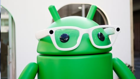 Green stylized Google Android mascot, white frame glasses, black eyes, alien ears