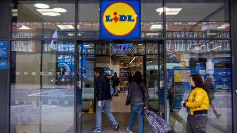 lidl store, glass wall and door, white woman in padded yellow winter jacket, shopping cart 