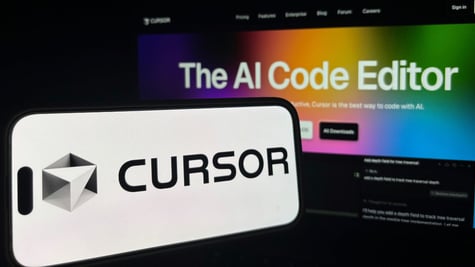 Cursor logo on phone, background AI coding agent written on computer screen.