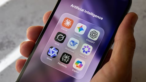 A hand holds a smartphone displaying the Claude, Gemini, ChatGPT and other AI apps