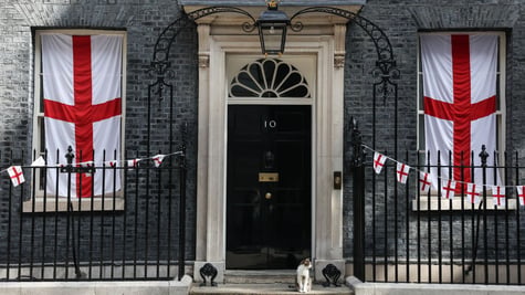 cat sits on doorstep, number 10 on door , flags in windows