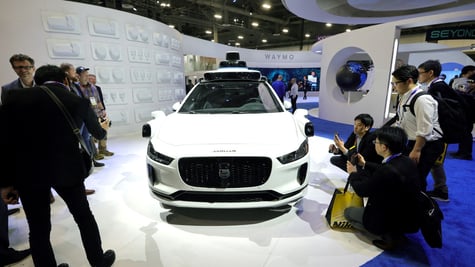 white Jaguar car on white pedestal, people around in black outfits take pictures of it 