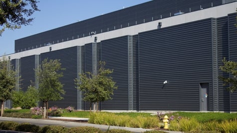 dark grey ai data centre building, some green grass, blue sky, five trees