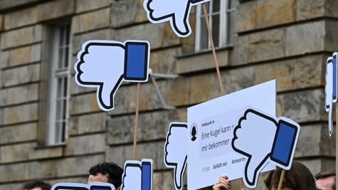 Protesters in Germany stand with their Facebook thumbs pointing down posters