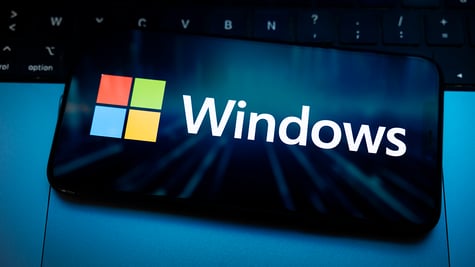 The Windows logo appears on the screen of a smartphone placed on a computer keyboard