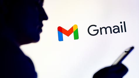 silhouetted individual is seen holding a mobile phone with a Gmail logo displayed in the background