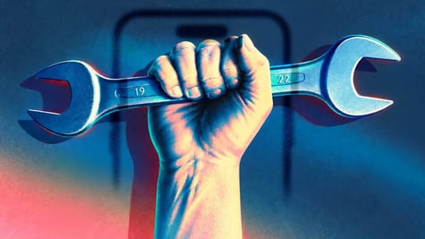 A hand holding a wrench with a smartphone in the background