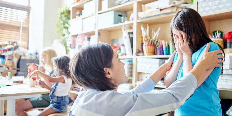 Side view of young female teacher comforting crying girl during lesson