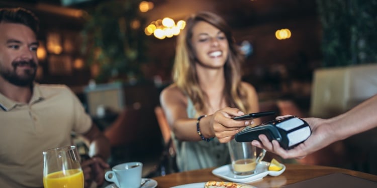 Happy couple using mobile phone and making contactless payment in a restaurant