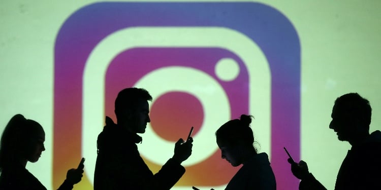Silhouettes of mobile users are seen next to a screen projection of the Instagram logo