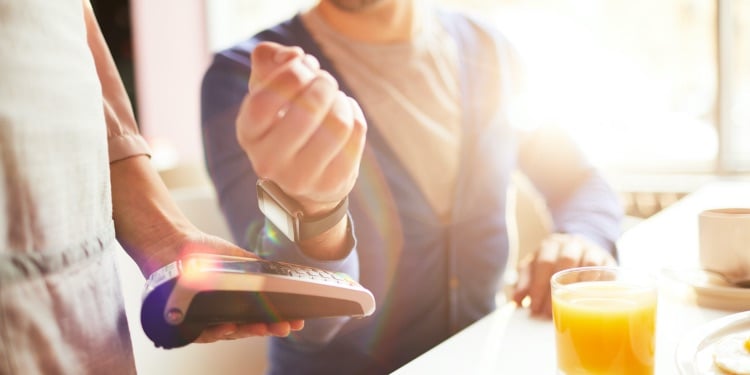 Hand of businessman with smartwatch over payment machine held by waitress