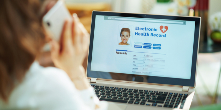 Seen from behind woman at home in sunny day using a cell phone and checking electronic health record