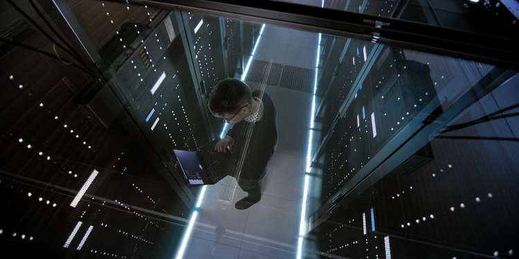 Top View Through the Glass of IT Engineer Working with Laptop in Data Center Full of Active Rack Ser