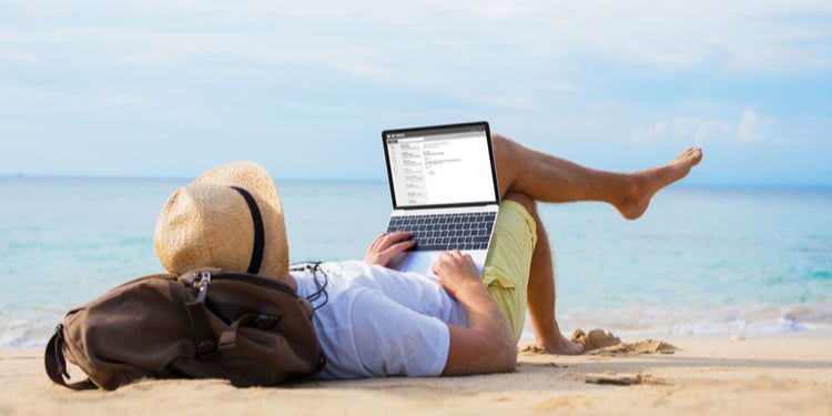 Man reading email on laptop while relaxing on beach