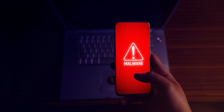 Hand holding mobile phone displaying malware warning with keyboard in background