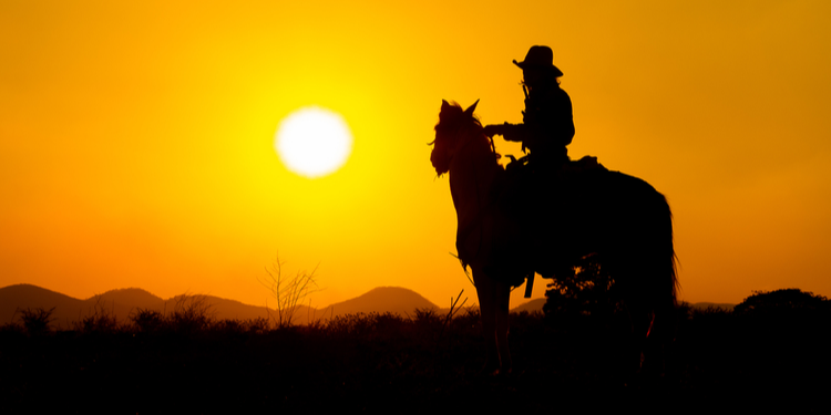 Silhouetted wild west outlaw on horseback silhouetted against sunset