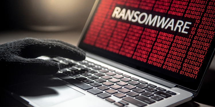 Hand with black glove typing on red matrix laptop screen with Ransomware inscription